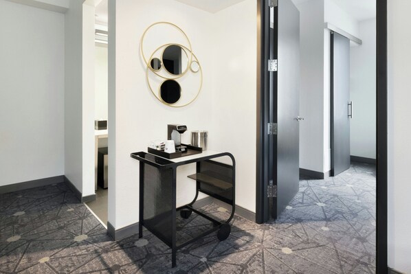 A modern bathroom with a black metal cart, a round mirror with a gold frame, and a patterned floor.