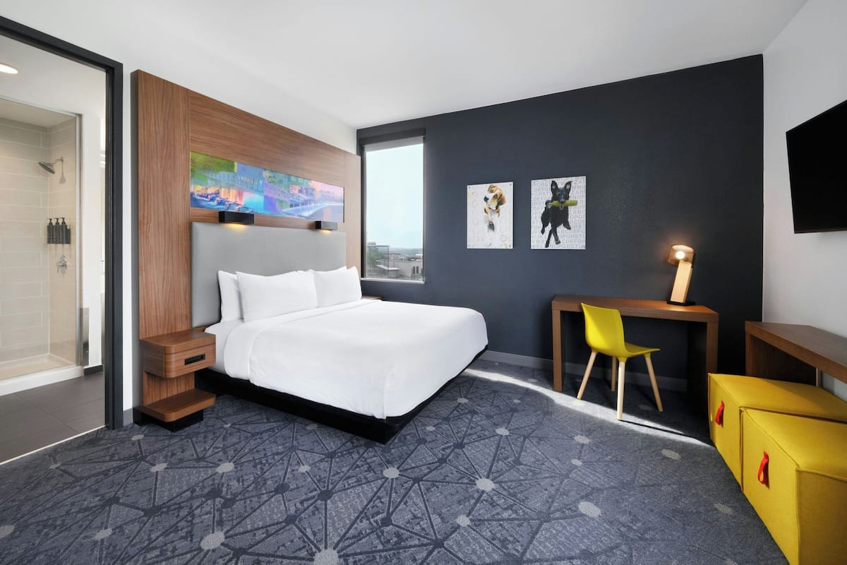 Una habitación de hotel moderna con una cama grande, un escritorio, una silla y un televisor.