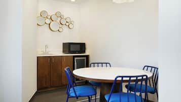 A conference room with a round table, blue chairs, a whiteboard, and a microwave on a cabinet.
