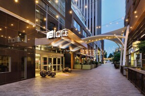 A hotel entrance with a modern design, featuring a prominent 'aloft' sign, a covered walkway, and decorative lighting.
