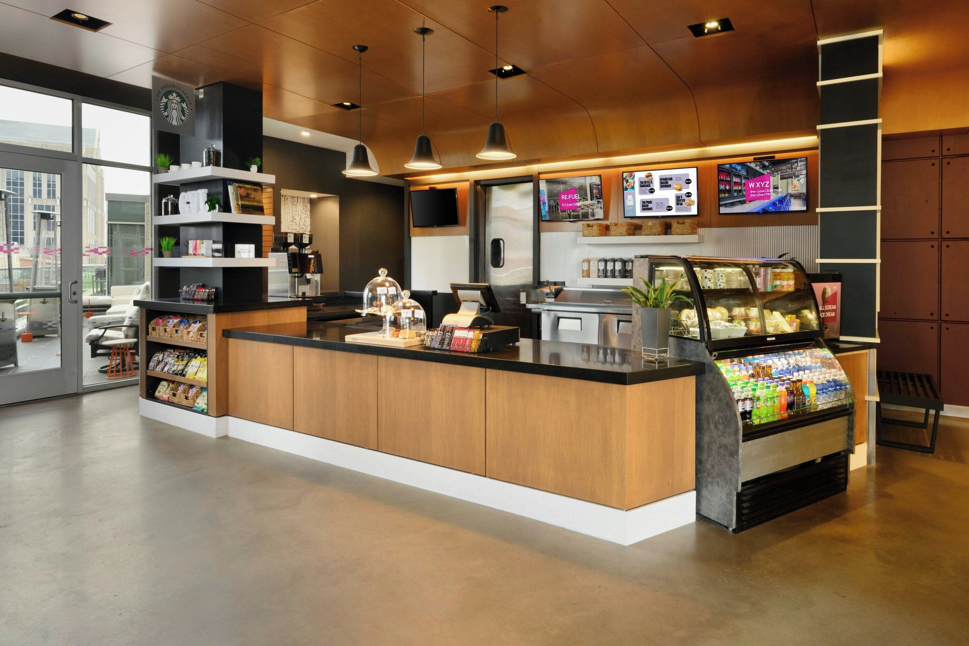 A modern coffee shop interior with a wooden counter, a refrigerated display case, and a digital menu board.