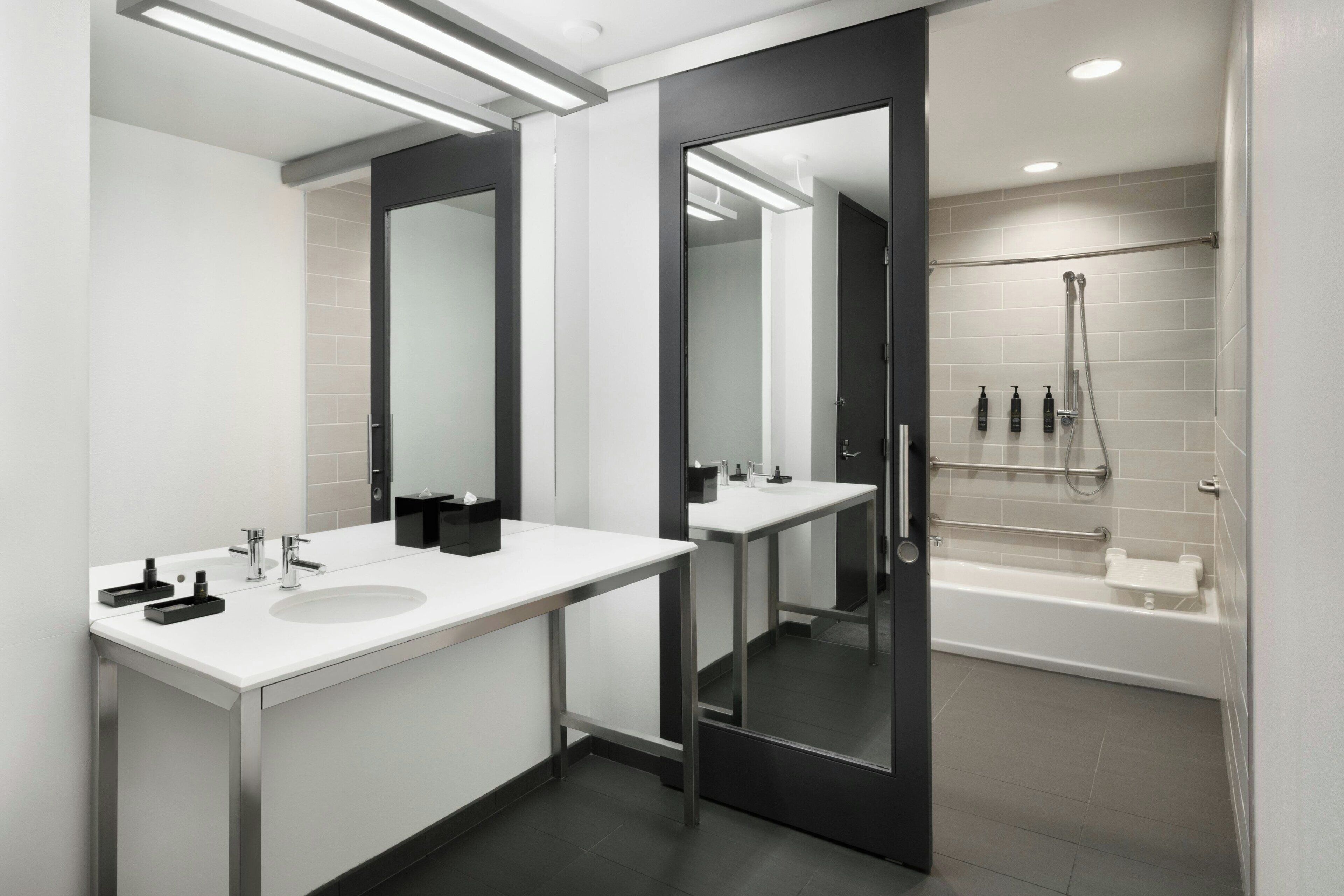 A modern bathroom with two sinks, a large mirror, and a walk-in shower.