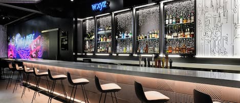 A bar area with a neon sign, bar stools, and shelves of bottles.