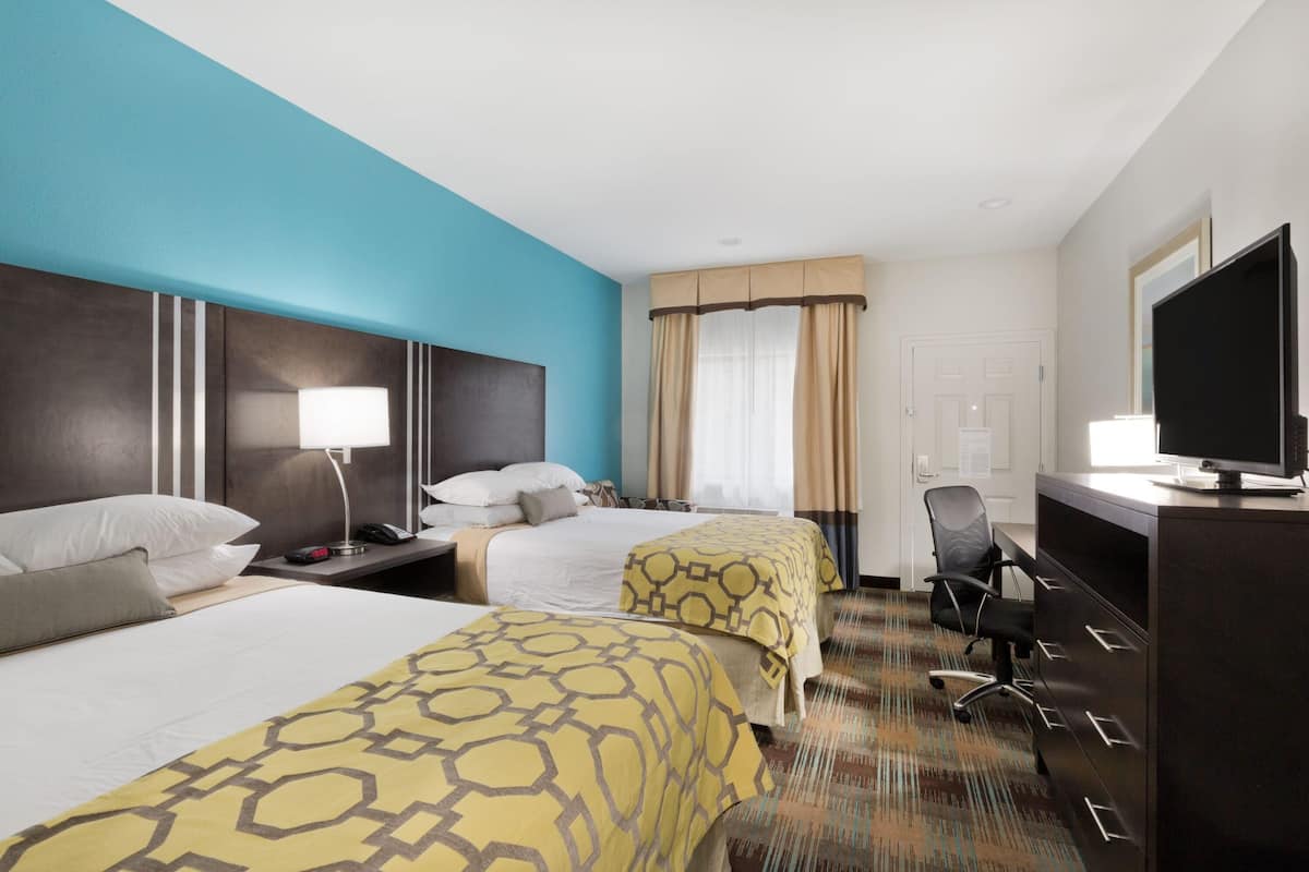 A hotel room with two beds, a desk, a chair, a television, and a window with curtains.