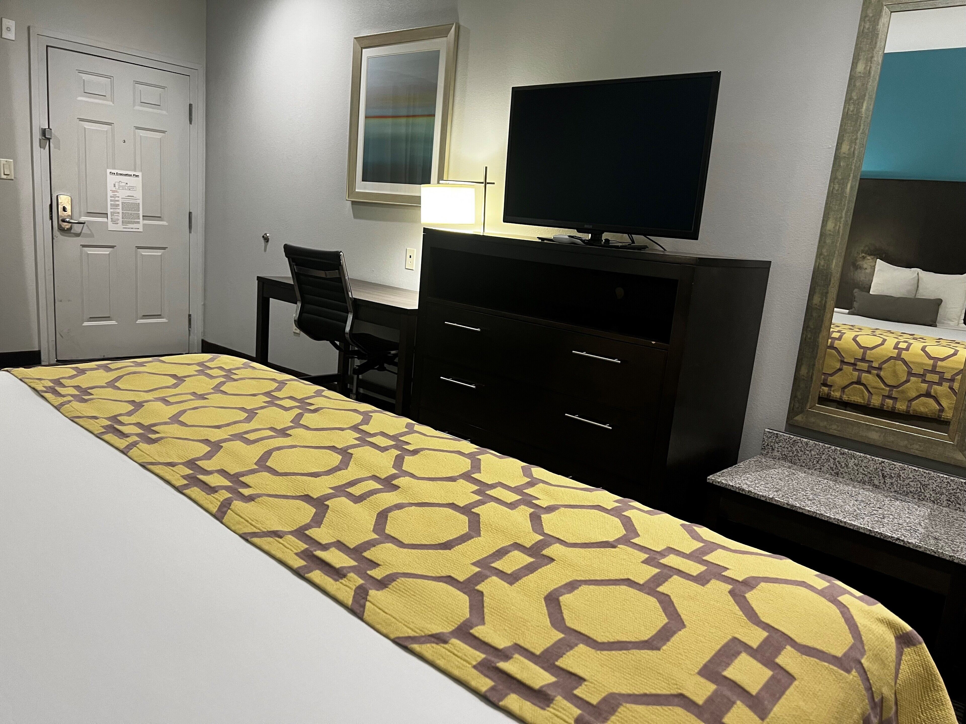 A hotel room with a bed, a desk, a chair, a television, and a mirror.