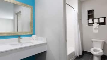 Un baño con un lavabo blanco, un espejo, una cortina de ducha, un inodoro y un estante con toallas dobladas.