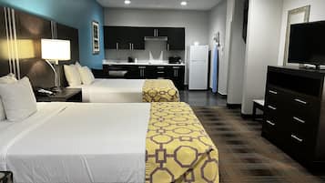 Habitación de hotel con dos camas, kitchenette, televisión y escritorio con lámpara.