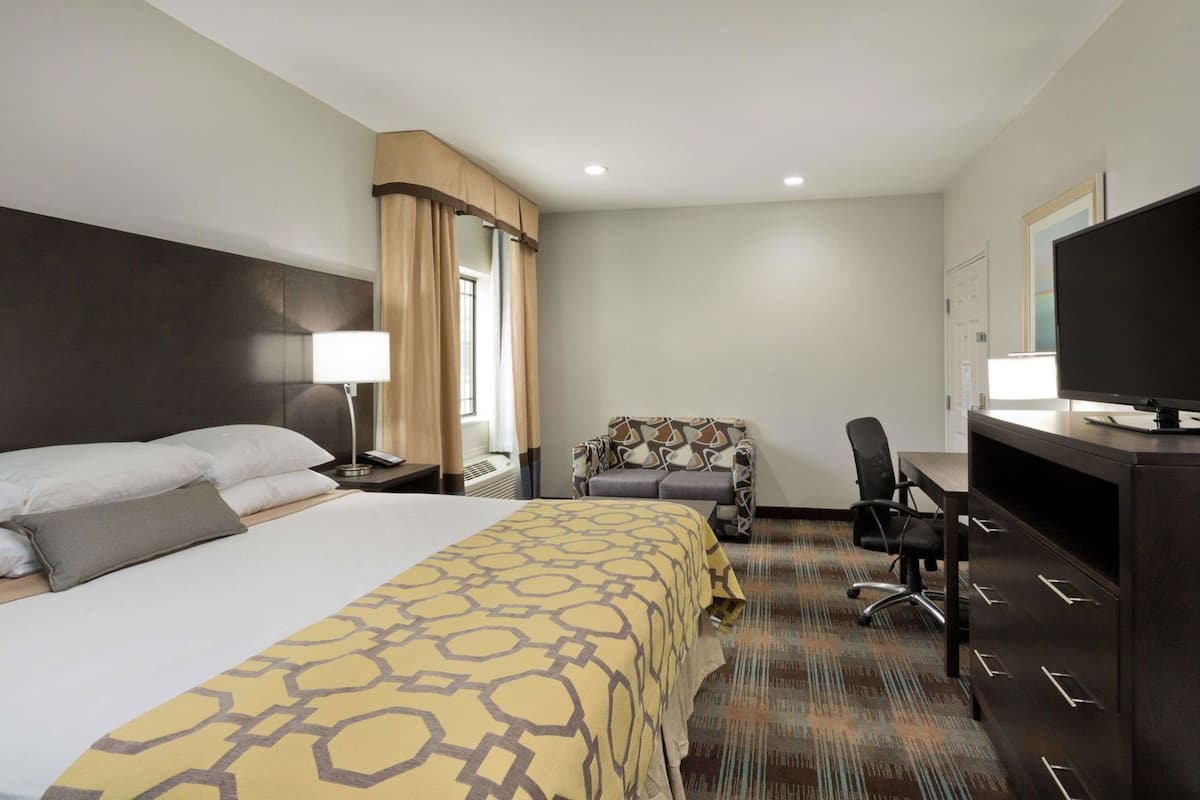 A hotel room with a bed, a desk, a chair, a television, and a window with curtains.