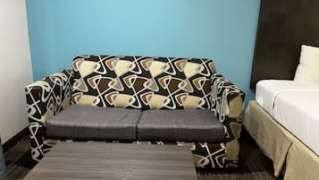 Una habitación con un sofá estampado, una mesita de madera y una cama.