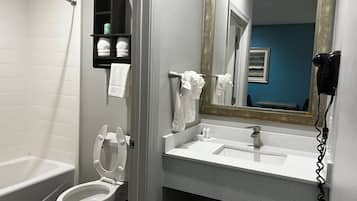 Un baño con inodoro blanco, lavamanos y espejo. Hay un perchero sobre el lavamanos y un estante con artículos de tocador.