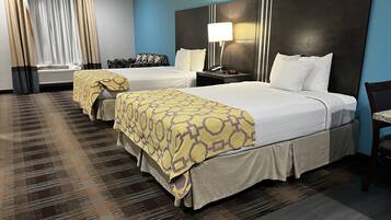 Habitación de hotel con dos camas, un cabecero grande, una mesita de noche con lámpara y una alfombra estampada.