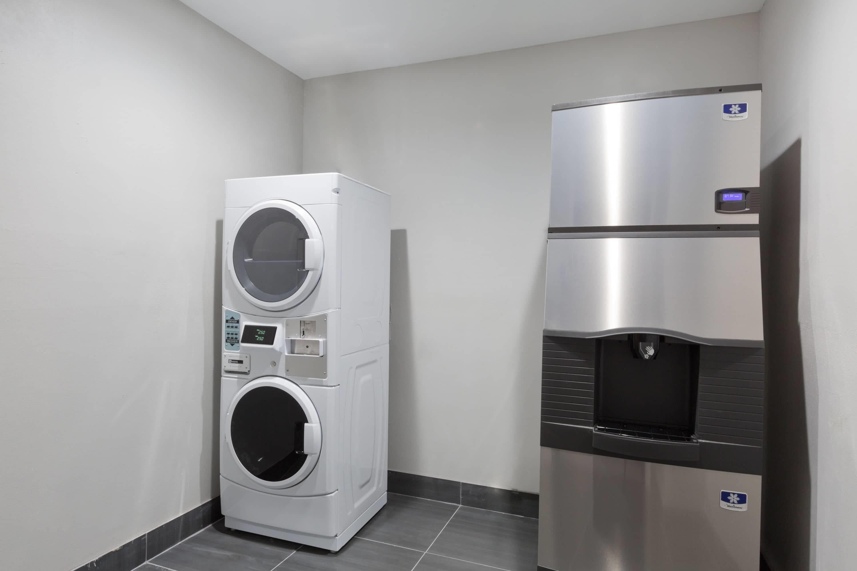 A laundry room with a stacked washer and dryer, a water dispenser, and a stainless steel refrigerator.