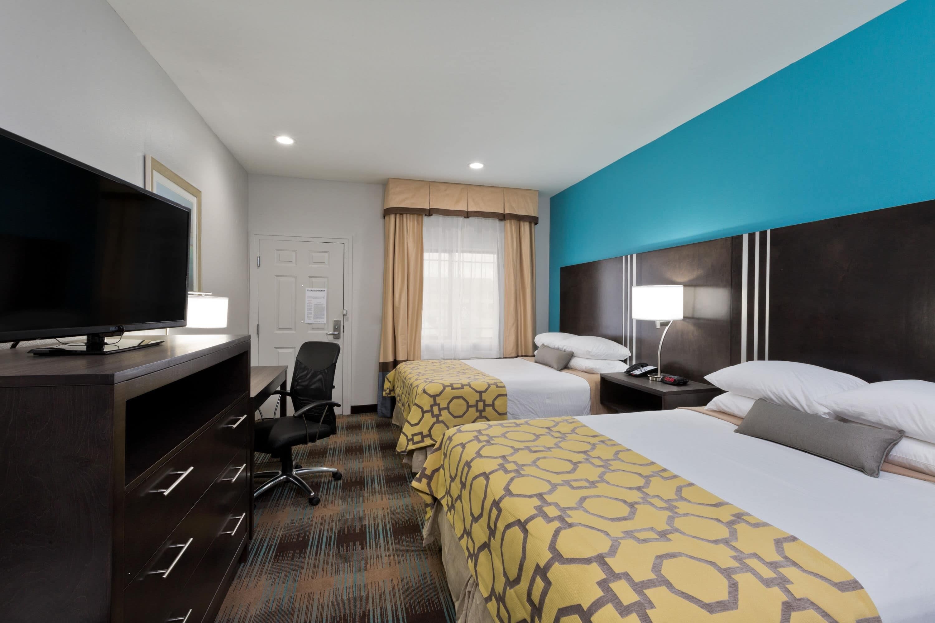 A hotel room with two beds, a TV, a desk, and a chair.