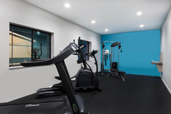 Un gimnasio con equipo de cardio, una banca de pesas y un soporte de pared.