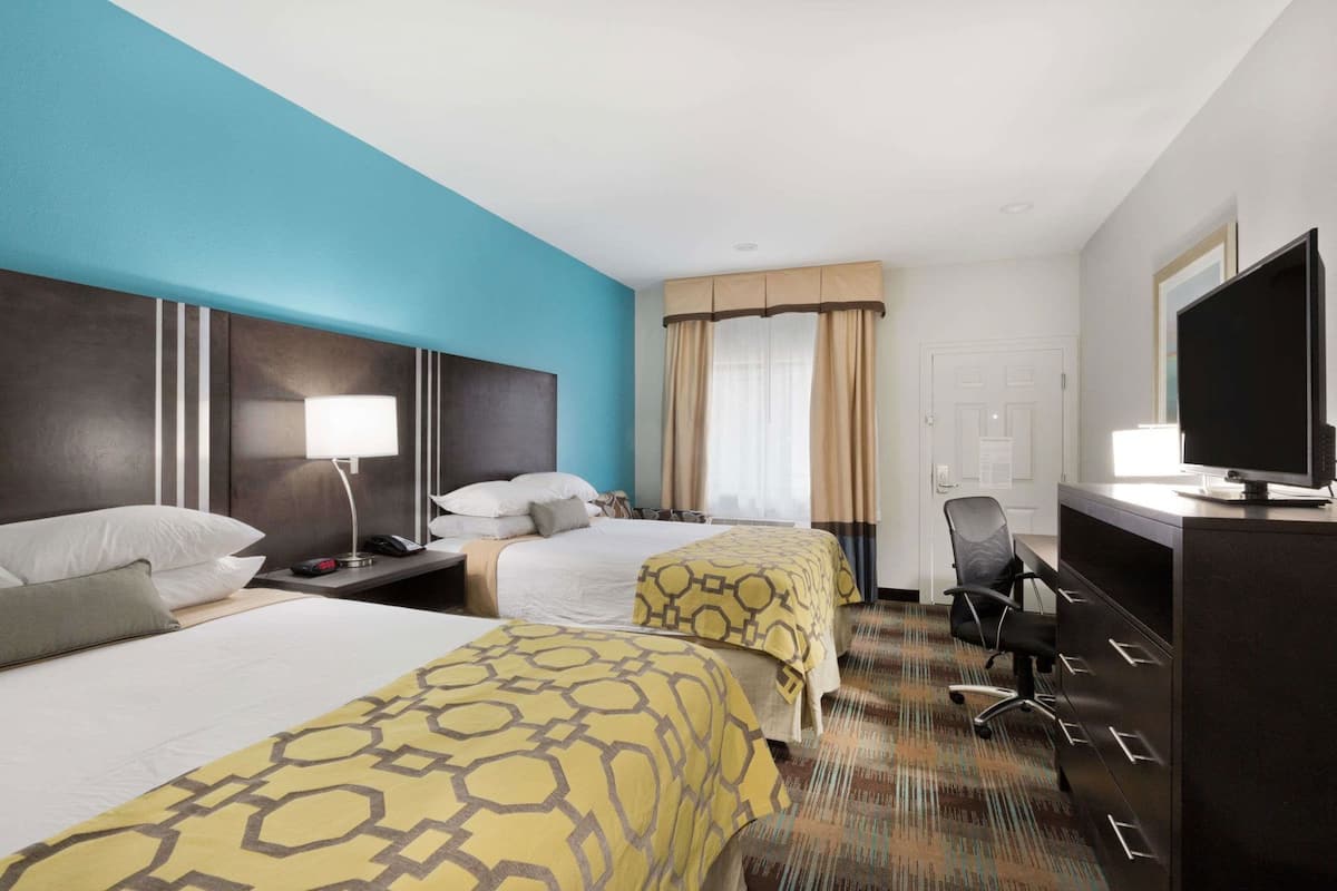 A hotel room with two beds, a desk, a TV, and a window with curtains.