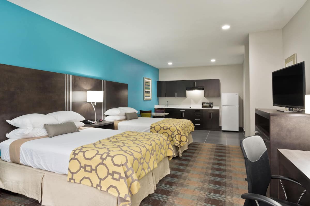 A hotel room with two beds, a desk, a chair, a television, and a kitchenette.