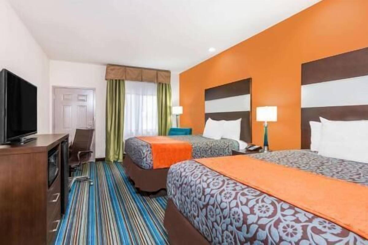 Una habitación de hotel con dos camas, un televisor, un escritorio y una alfombra a rayas.