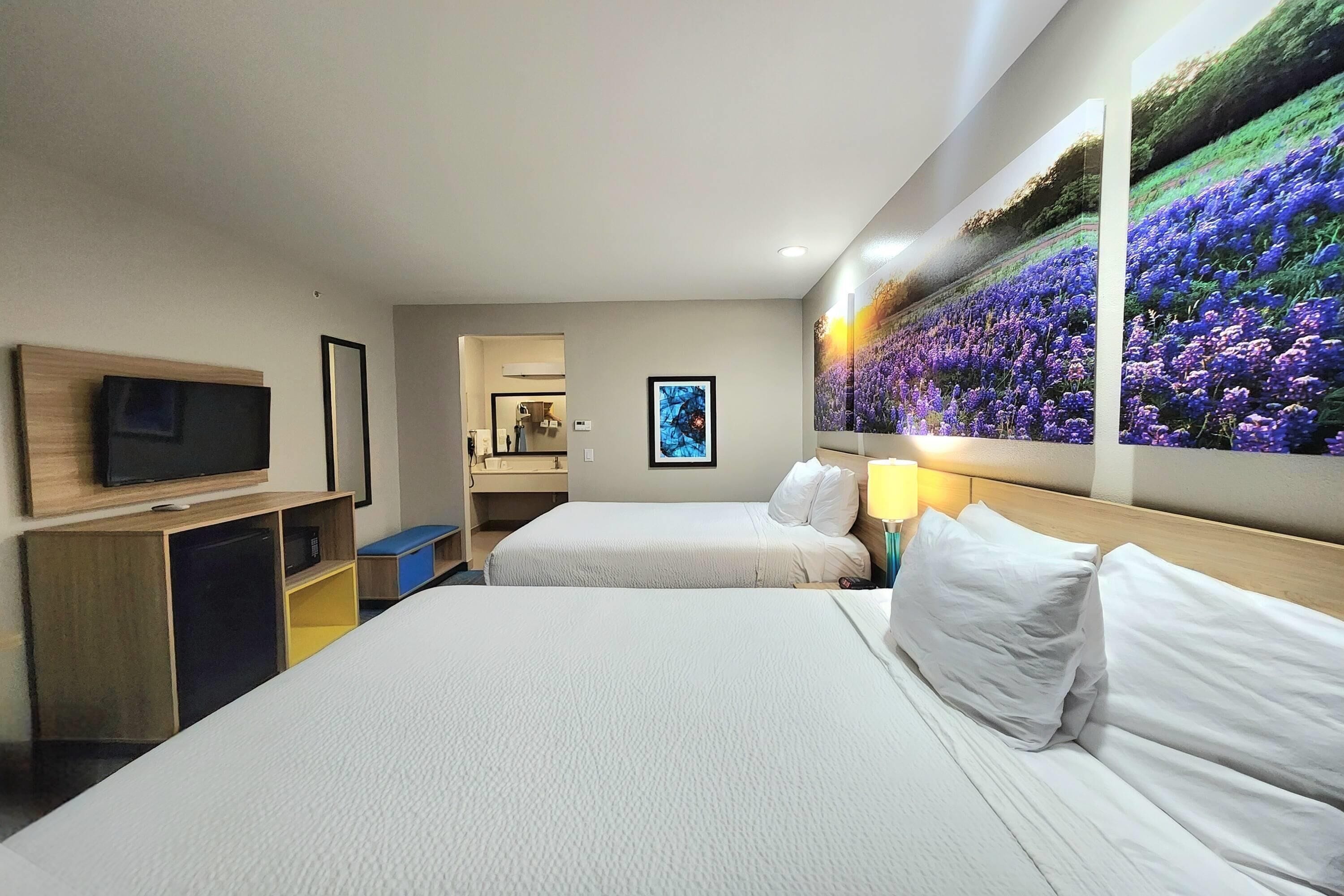 Une chambre d’hôtel avec deux lits, une télévision, un bureau et un tableau représentant des fleurs accroché au mur.