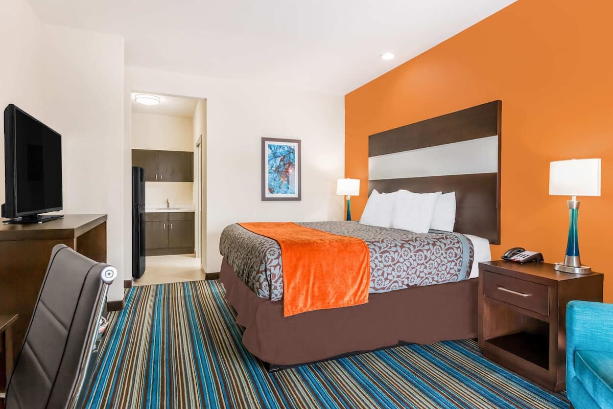 Habitación de hotel con cama, mesita de noche con lámpara, televisor y vistas al pasillo.