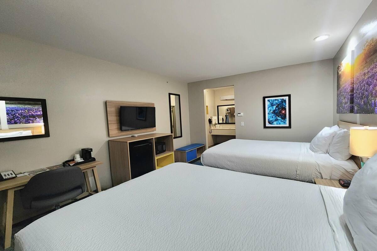 Una habitación de hotel con dos camas, un escritorio con ordenador, televisor y espejo.