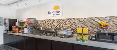 Un área de desayuno con un letrero que dice "Daybreak Breakfast", equipada con cafeteras, un tostador y varios recipientes de comida.
