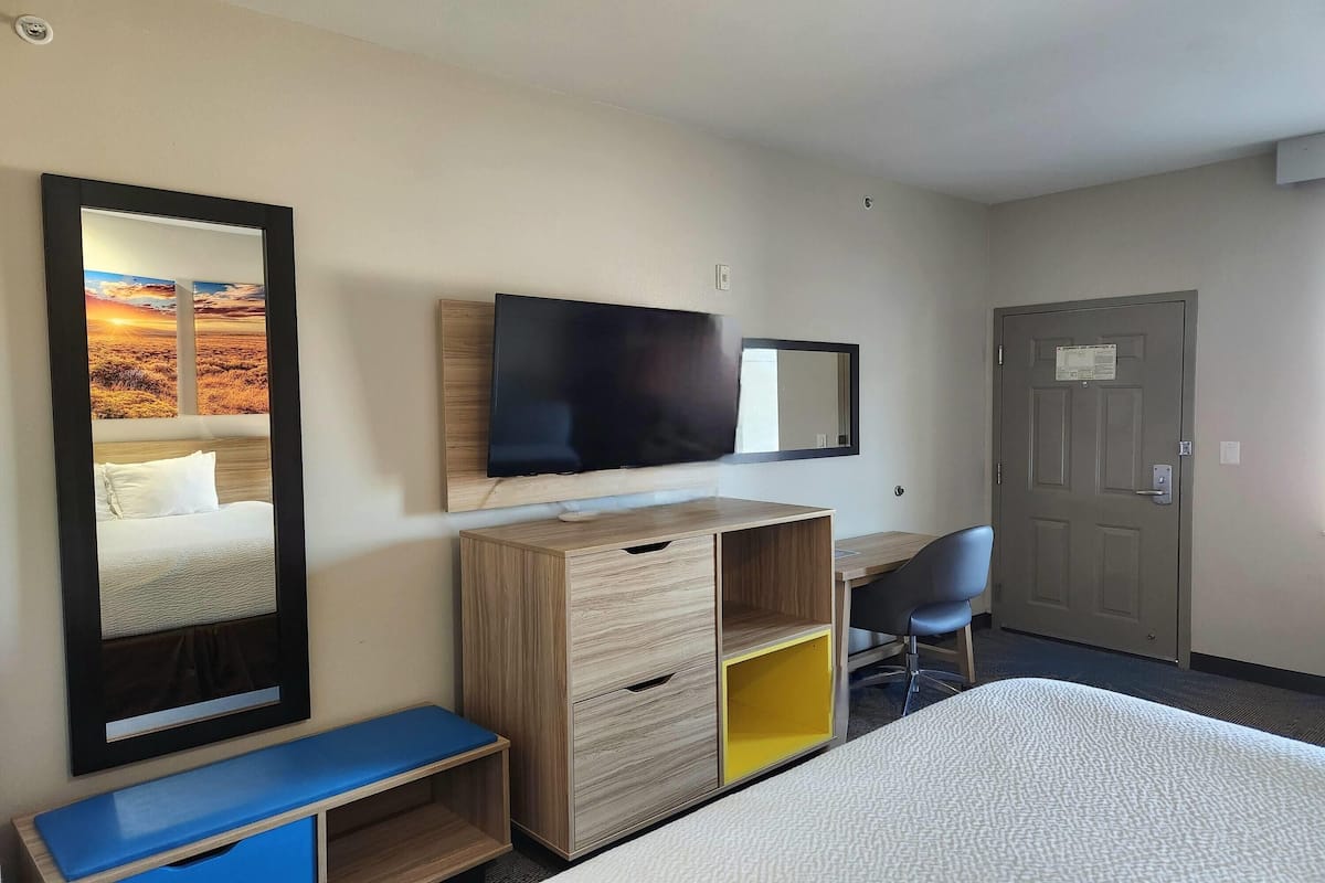 Habitación de hotel con cama, escritorio, silla, televisor, armario y puerta.