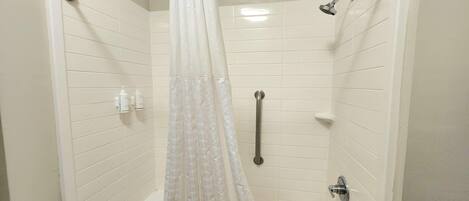 A shower with a white curtain, a handheld showerhead, and a wall-mounted faucet.
