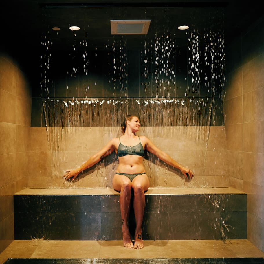 A woman sitting in a shower with water falling around her.