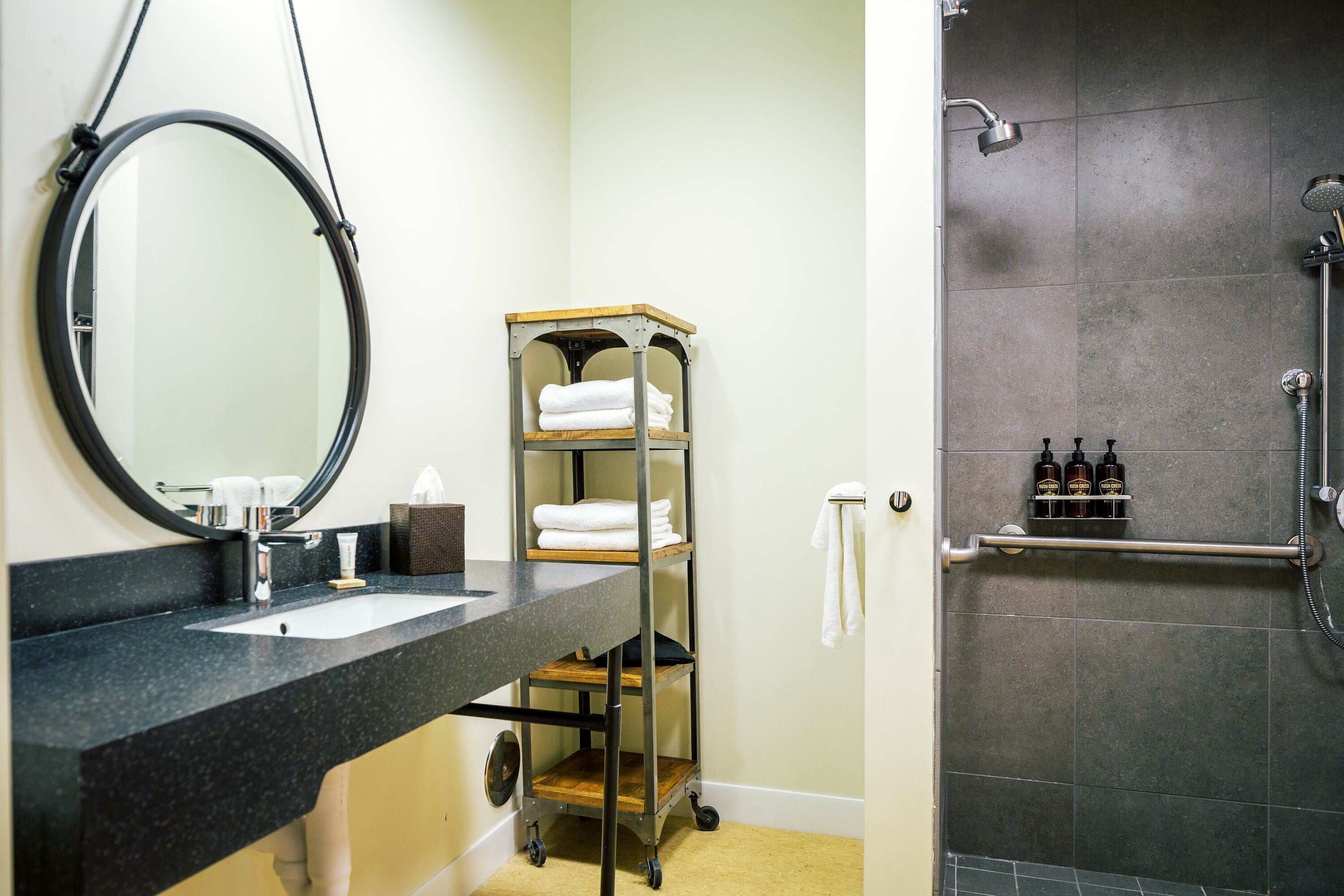 A bathroom with a sink, mirror, towel rack, and a shower area.