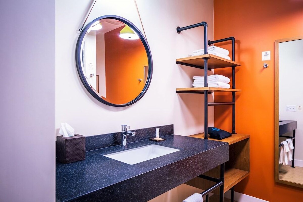 Un baño con un espejo redondo, un lavamanos y un estante con toallas.