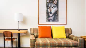 A room with a plaid sofa, a wooden desk, a chair, and a framed picture of a wolf on the wall.