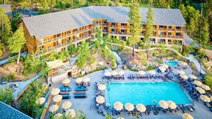 A resort with a large pool, outdoor seating, and a wooded area.