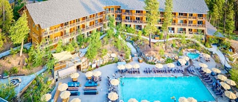 A resort with a large pool, outdoor seating, and a wooded area.