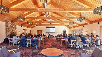 Une salle de conférence avec des poutres en bois, des tables rondes et des chaises disposées pour une réunion.