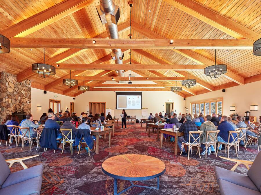Une salle de conférence avec des poutres en bois, des tables rondes et des chaises disposées pour une réunion.