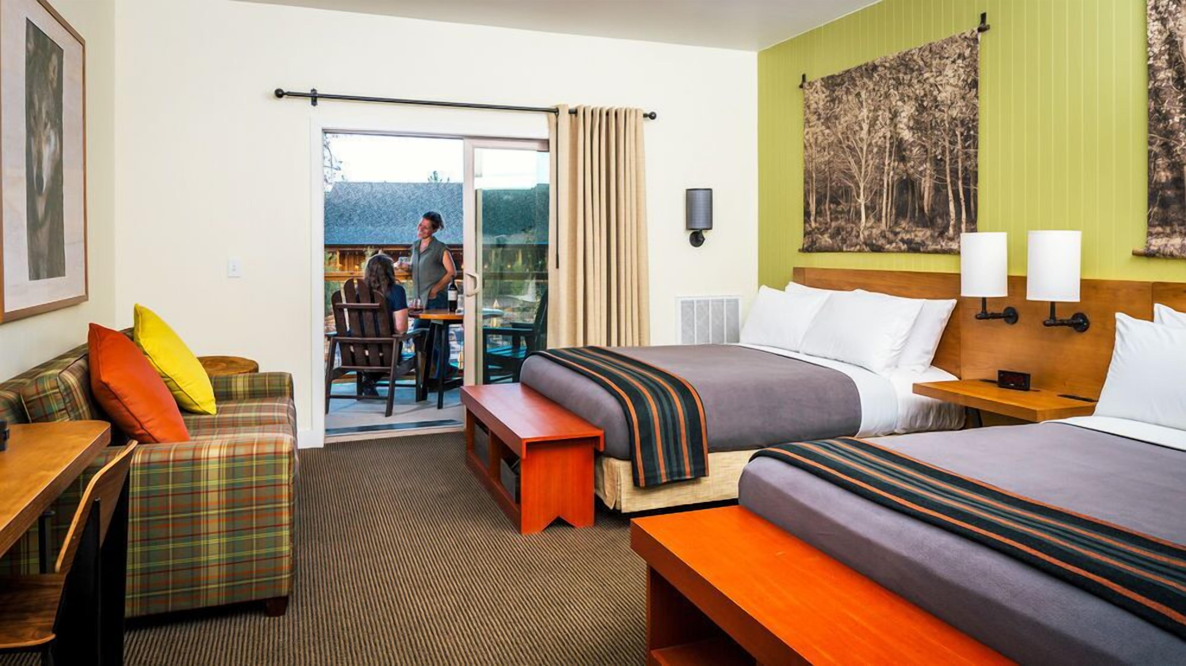 A hotel room with a bed, a sofa, a small table, a bench, a desk, and a view of the outside.