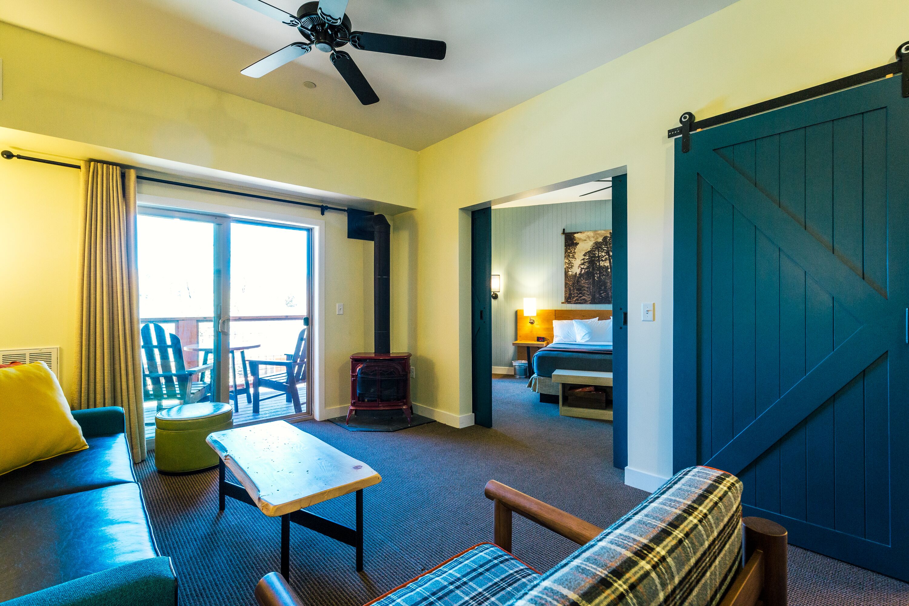 Une chambre d’hôtel équipée d’un canapé, d’une table, d’un fauteuil à motifs, d’un lit, d’une porte coulissante et d’un ventilateur de plafond.