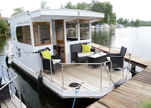 A white river cruise boat with a covered deck, wicker furniture, and a small table.