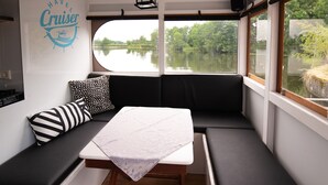 A cabin with a bed, a table, and a view of a lake. - HAVEL Cruiser (Brandenburg an der Havel)