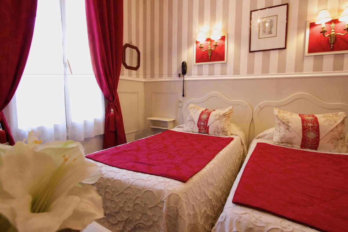A hotel room with two beds, red and white bedding, a telephone on the wall, and striped wallpaper.