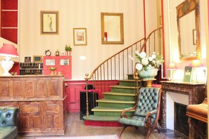 Ein traditionelles Interieur mit Treppe, einem grünen Polsterstuhl, einem Holztisch und einem Kamin.