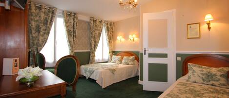 A hotel room with two beds, a desk with a chair, a television, and a chandelier.