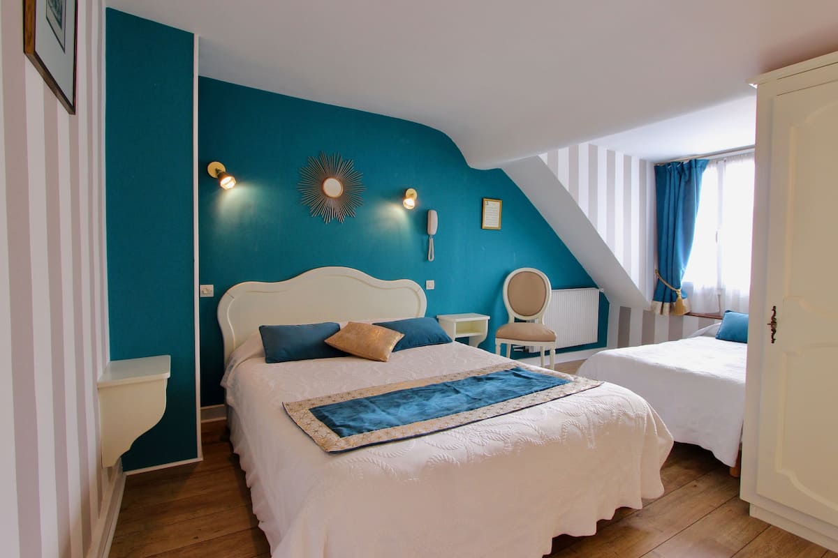 A bedroom with a large bed, a smaller bed, a chair, a nightstand, and a wall-mounted light fixture.