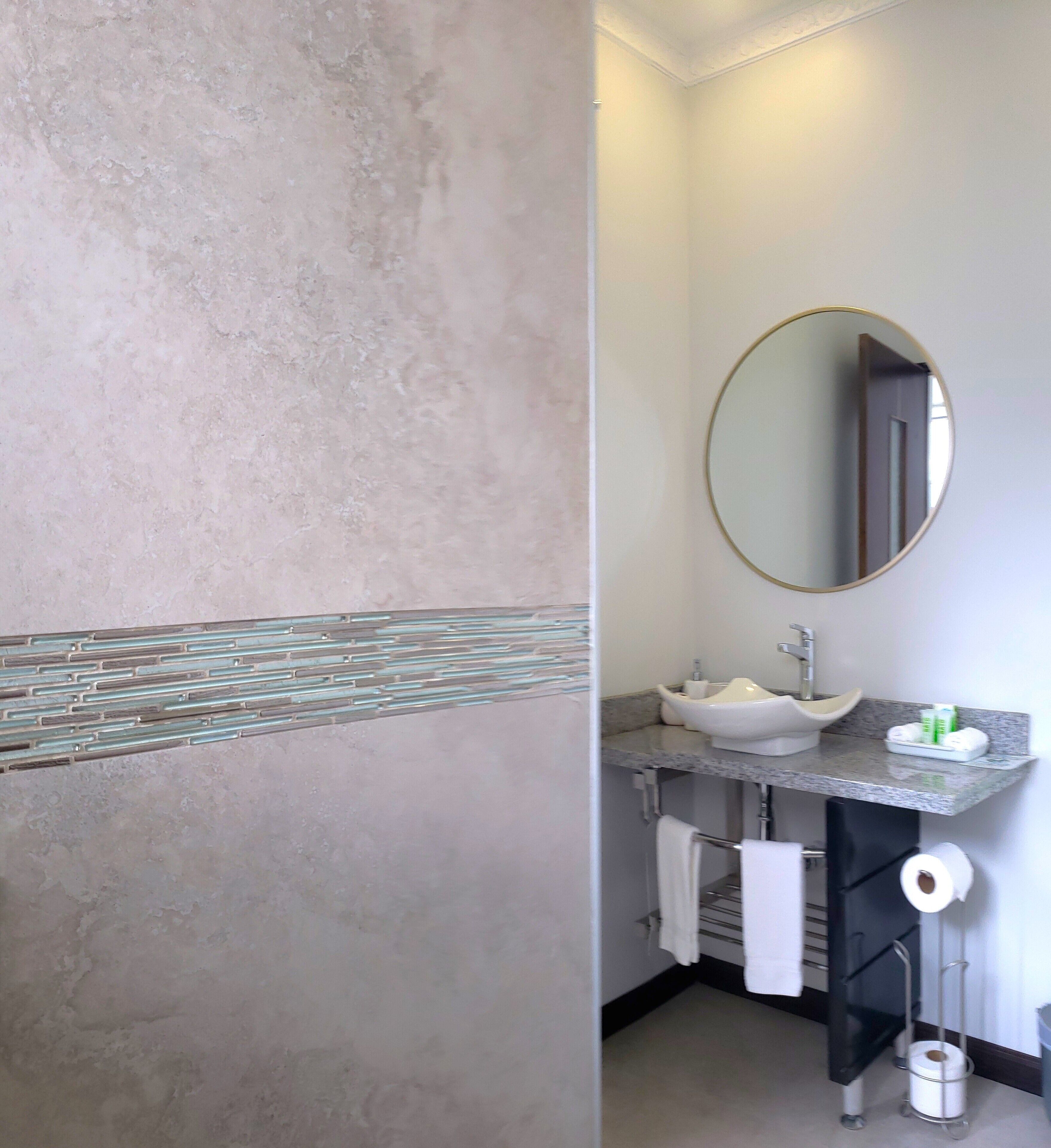 A bathroom with a marble wall, a round mirror, a sink with a vessel basin, and a towel rack.