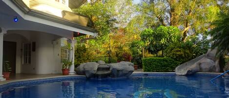 Una piscina con una cascata, circondata da grandi rocce e rigogliosa vegetazione.
