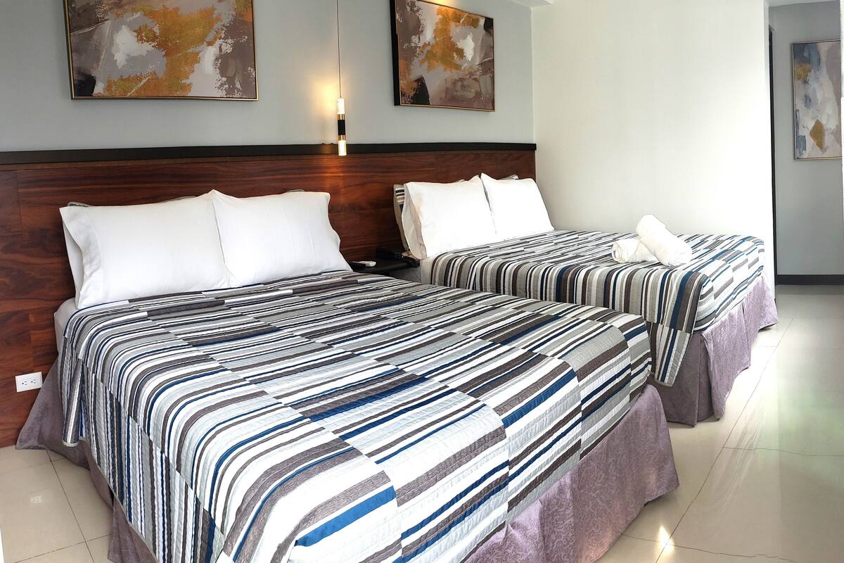 Ein Hotelzimmer mit zwei Betten, jeweils mit gestreifter Bettwäsche, einem Holzkopfstück und Bildern an der Wand.