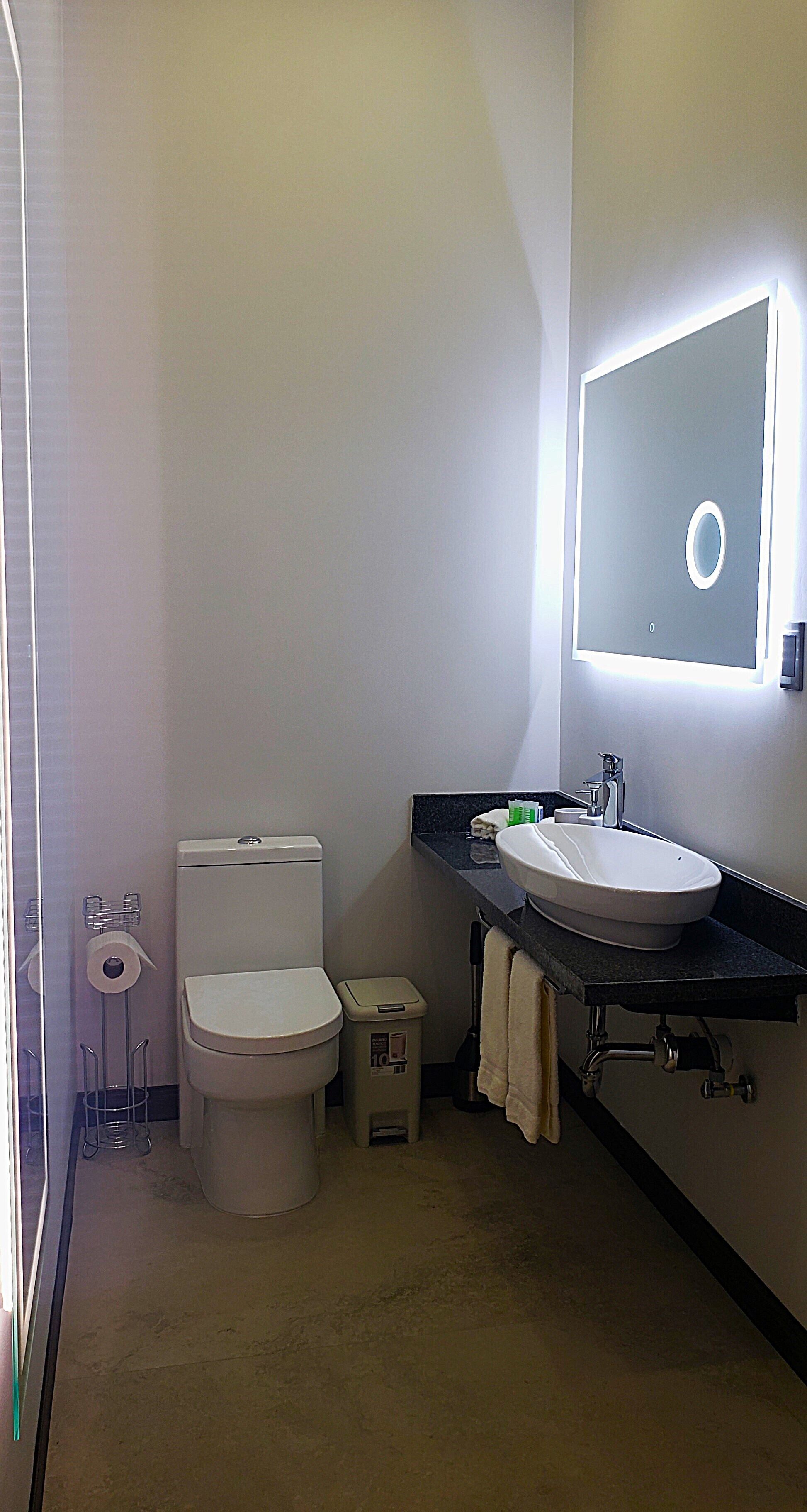 Un baño pequeño con inodoro, lavamanos y espejo con luz.