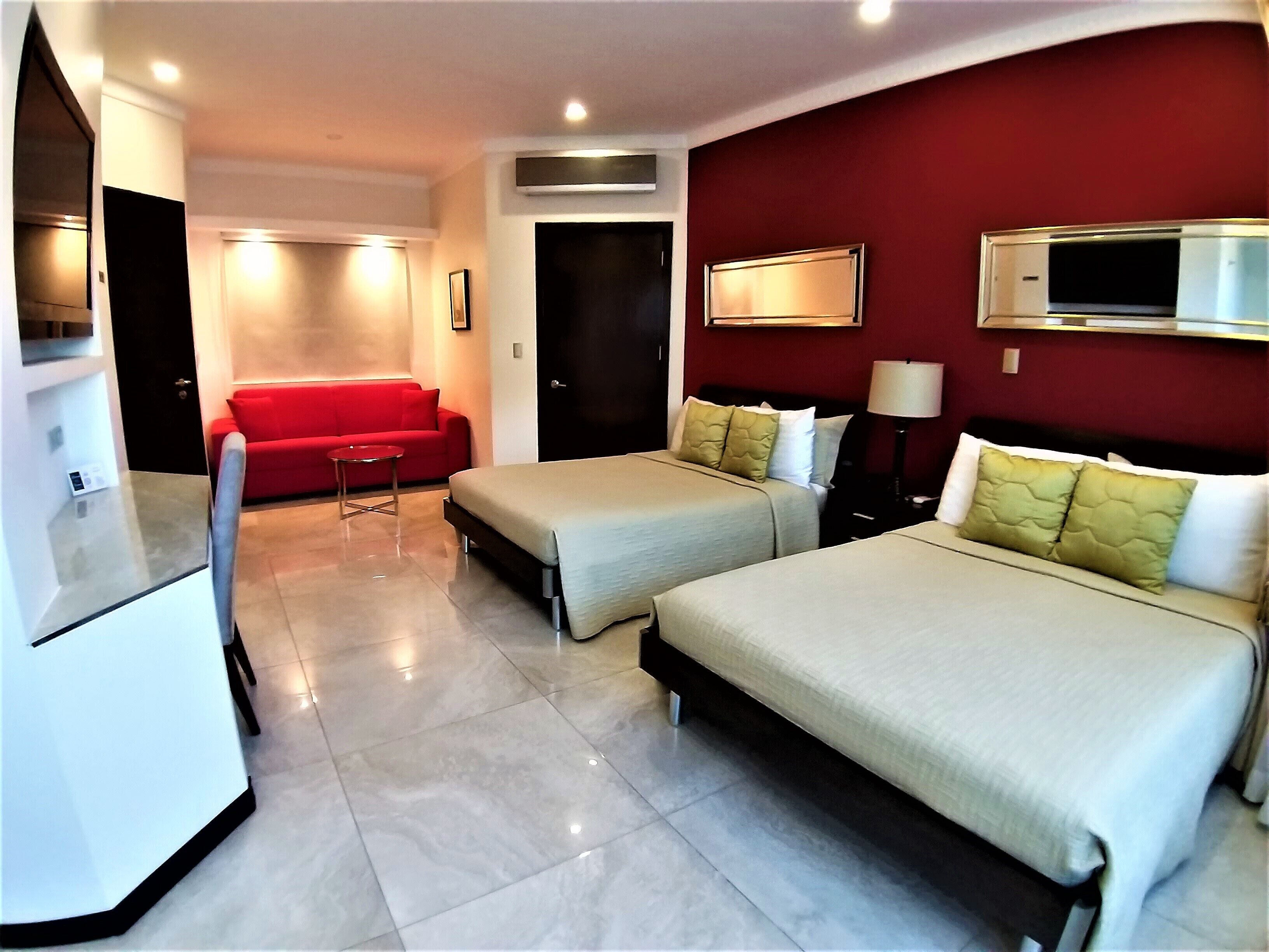 A hotel room with two beds, a red sofa, a TV, and a microwave.
