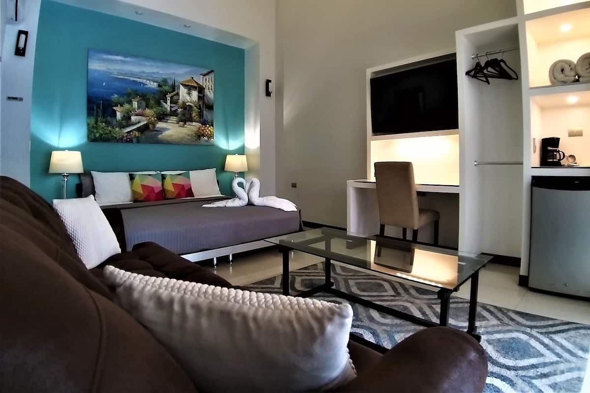 Ein modernes Hotelzimmer mit Bett, Glastisch, Schreibtisch und Fernseher.