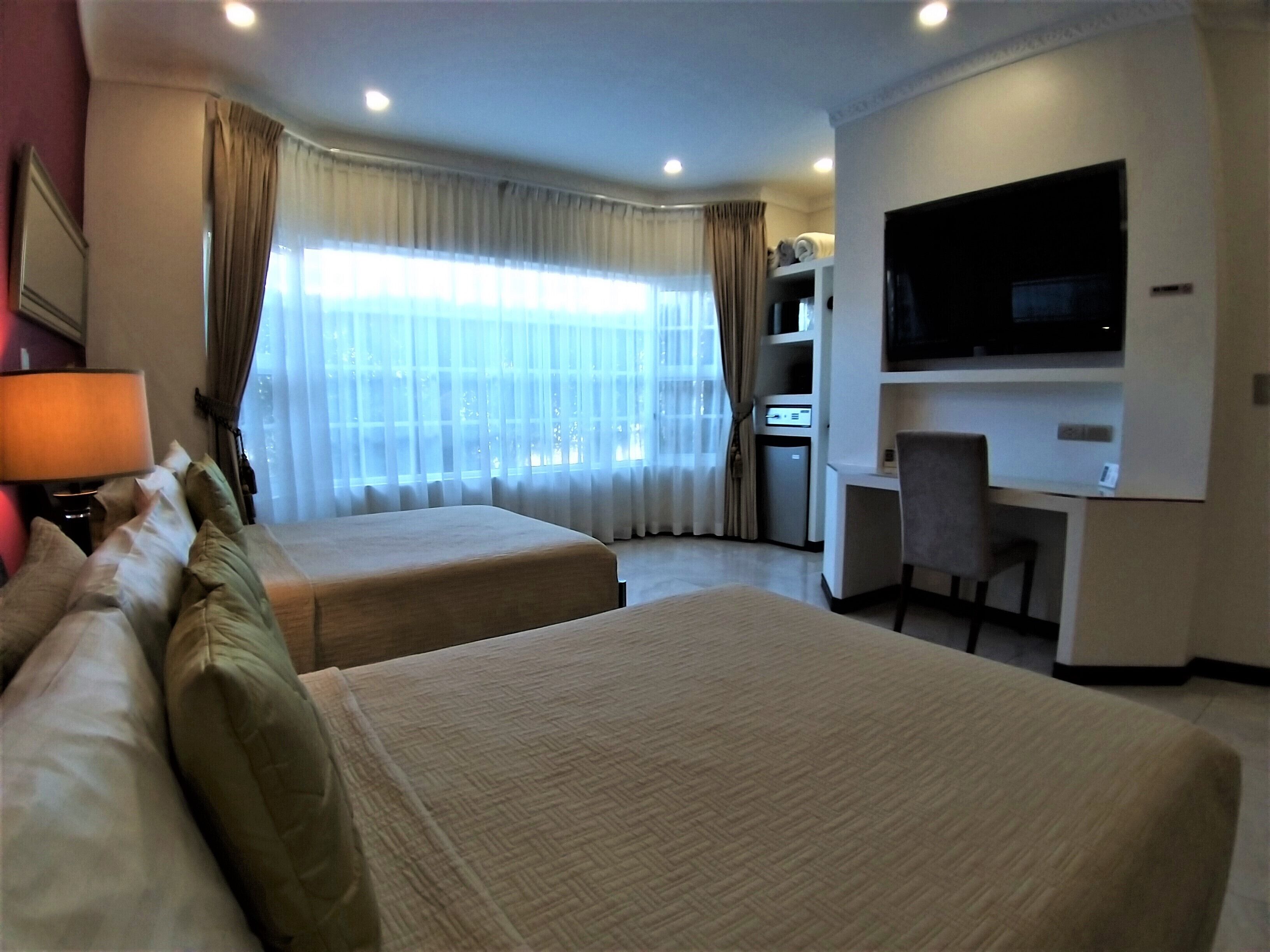 Een hotelkamer met twee bedden, een bureau, een televisie en een minibar.
